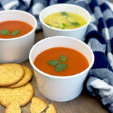 Three bowls of soup with crackers on a wooden surface