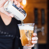 16 oz plastic cup with "Island Time" logo filled with beer poured from "Hi-Neighbor!" can, held by person in black shirt, bar in background