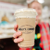 20 oz plastic coffee cup with black "Molly's Corner" logo, filled with milky coffee and white froth, held by person in red vest