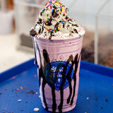 20 oz plastic cup with blue "Sweet Harbour" logo, filled with pink smoothie, whipped cream, chocolate, sprinkles, and chocolate syrup, on blue tray in cafe
