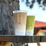 Two drinks in clear plastic cups on a wooden surface with a blurred natural background