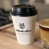 8 oz paper cup with black dome lid, printed "Suited Coffee" logo, on wooden tray next to espresso shot in glass cup