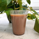 Coffee drink in blank 7 oz plastic cup on white table with plant in background