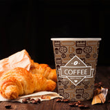 12 oz. Full Wrap Recyclable Paper Cup displaying "coffee", on a wooden table, with coffee beans sprinkled around, beside a croissant,