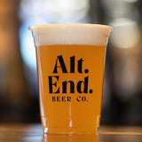 16 oz plastic cup with black "Alt End Beer Co" logo, filled with beer with froth, standing on wooden table