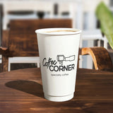 16 oz double walled paper cup, with a black text logo "Coffee Corner", filled with coffee, on a wooden table