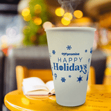 16 oz paper cup with blue "Happy Holidays" text and snowflakes, with animated steam, on table next to book, cafe in background