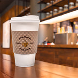 16 oz paper cup with white dome lid and brown sleeve printed "Premium Arabica" with cup graphic, on coffee bar table, coffee supplies in background