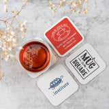 Four coasters of varying designs with a cup of tea on a white marble background