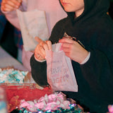 White paper sandwich bags featuring a festive "Merry and Bright" print, filled with assorted candies and displayed buffet-style on a table for party favors.