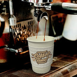 White paper coffee cup with a white coffee sleeve featuring "Coffee Time!" logo, filling with a espresso shot
