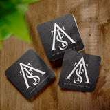 Three black square coasters with "As The Structure Falls" logo on a wooden table