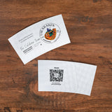Two custom coffee sleeves on a wooden surface, one with a logo and text, the other with a QR code