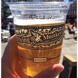 12 oz plastic cup filled with beer with Flying Monkeys banner, held by hand, with busy street in background