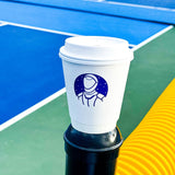 12 oz double-walled paper cup with white dome lid, astronaut and star logo in blue, standing on black pole, tennis court in background