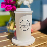 16 oz paper cup with "Vintage Road Coffee Co" circular logo, on white coaster on table next to bowl of flowers, hand reaching to grab cup