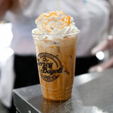 24 oz plastic cup with black "Jersey Bagels" text, filled with iced cream coffee, whipped cream and caramel sauce, on metal table