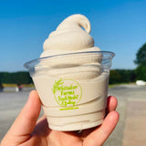 9 oz plastic cup with Whitaker Farms logo, filled with soft serve ice cream, held by hand in park setting