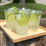 Five 10 oz recyclable plastic cups with clear drinks, lime, ice, and mint on wooden tray outdoors