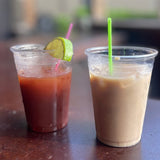 Two 10 oz plastic cups filled with cream and red drinks, garnished with colorful straws, on wooden bar table
