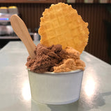 5 oz paper food container, filled with ice cream, with a waffle and a wooden spoon, on white table in a cafe