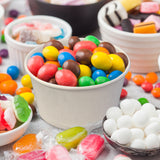 5 oz paper food container, filled with chocolate candy eggs, surrounded by confectionary in bowls and plates