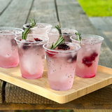 Blank 7 oz recyclable plastic cups with pink drink, herbs and berries on wooden tray