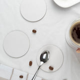 Three blank medium weight round coasters with a metal spoon, coffee cup and coffee beans on a white table