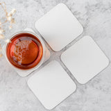 Four 4" Blank Medium Weight Square Coasters with a cup of tea resting on one, with a white marble background