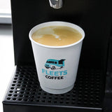 12 oz double-walled paper cup with "Fleets Coffee" logo and van graphic in black and blue, filled with milk coffee with foam, standing in coffee machine