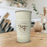20 oz paper cup with white sleeve printed "Organic Cafe" in brown with circle logo, on wooden table, cafe bar in background