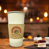 20 oz paper cup with brown sleeve printed "Premium Quality" and cup logo, on wooden table next to tray with three small desserts, cafe in background