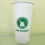 20 oz paper cup with green "The Stable" text and sports logo, standing on light green surface