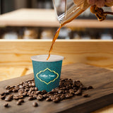 4 oz. Full Wrap Recyclable Paper Cup, displaying "Coffee Time" logo, pouring espresso, on a wood board surrounded by coffee beans, on top of a wooden table.