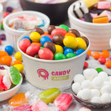 5 oz paper food container, with pink and yellow "Candy Shop" print, filled with candy, on a table surrounded by confectionery
