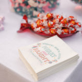 Stack of White Paper Sandwich Bags with "Merry and Bright" print, in front of a candy platter, on a white cloth table