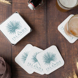 Five white square coasters with printed with a green leaf fan and "The Islands of Islamorada" logo on a wooden table, with one of two beer glasses on a coaster