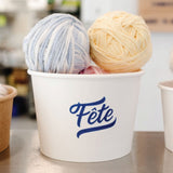 16 oz paper food container, with blue "Fete" logo, filled with three balls of yarn, on a table