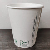 12 oz compostable paper cup with green "SFI" text, on grey wooden table with white wall background