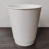 Blank white 12 oz premium double walled paper cup on grey wooden table, white wall in background