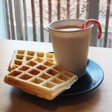 12 oz paper cup with coffee and lollipop, on blue plate with two waffles, on table, window in background