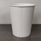 Blank white 4 oz paper cup showing seam, on grey wooden table, white wall in background