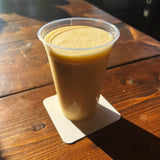 20 oz plastic coffee cup filled with creamy coffee, on white square coaster, standing on wooden table