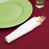 Blank 3-PLY White Dinner Napkin wrapped around a gold cutlery set, next to a green plate on a red table cloth